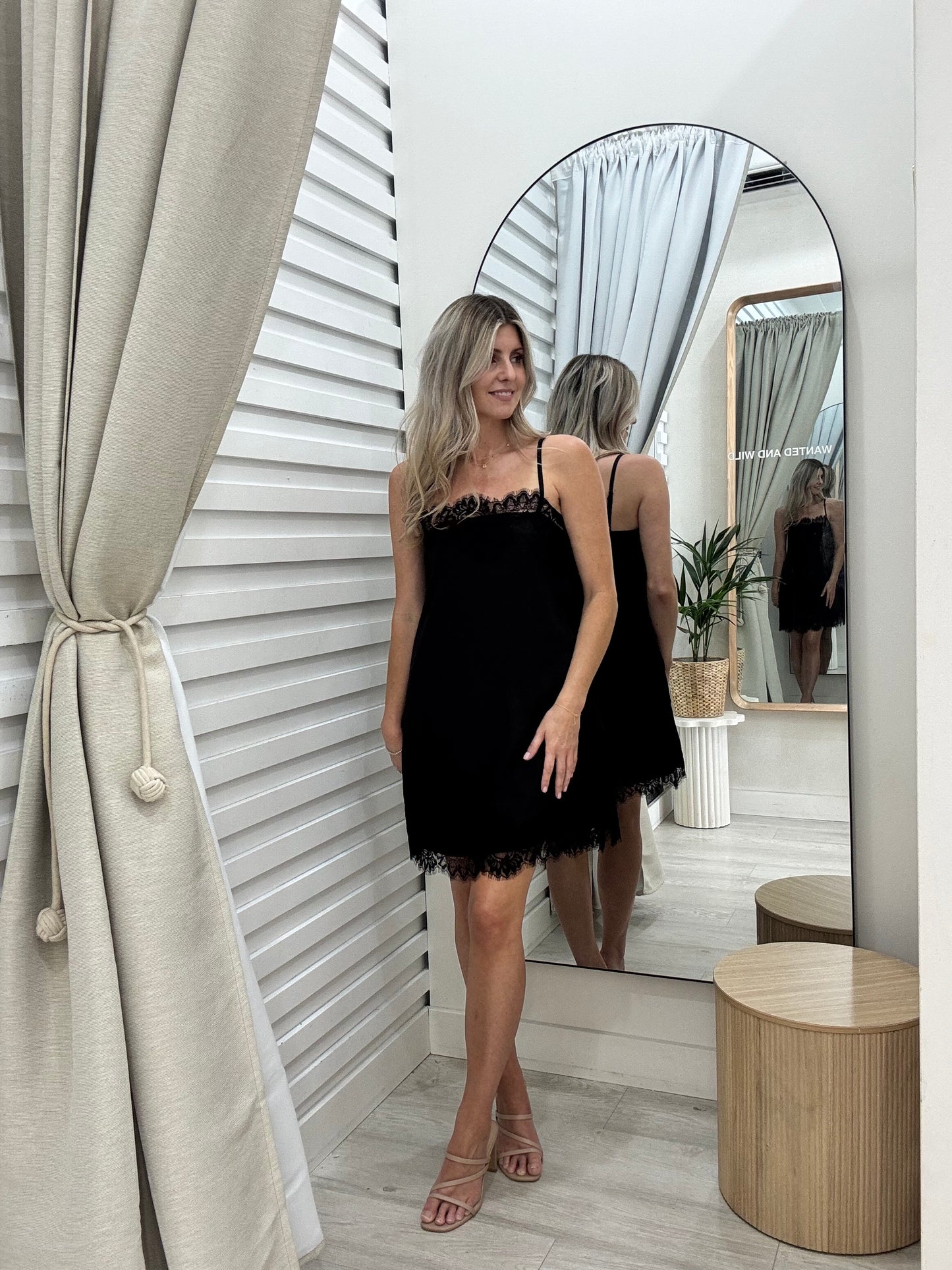 A woman in the Ace dress in black. By Frankie label standing in front of a mirror in the changeroom of Wanted and Wild Gymea.