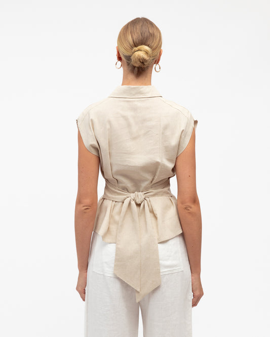 Woman wearing a beige sleeveless shirt with a tie waist on a white background. Back view