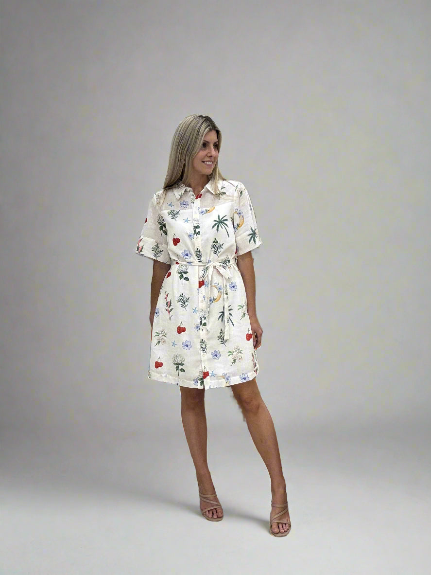 Woman in a patterned dress standing in front of a large mirror with a neutral curtain.
