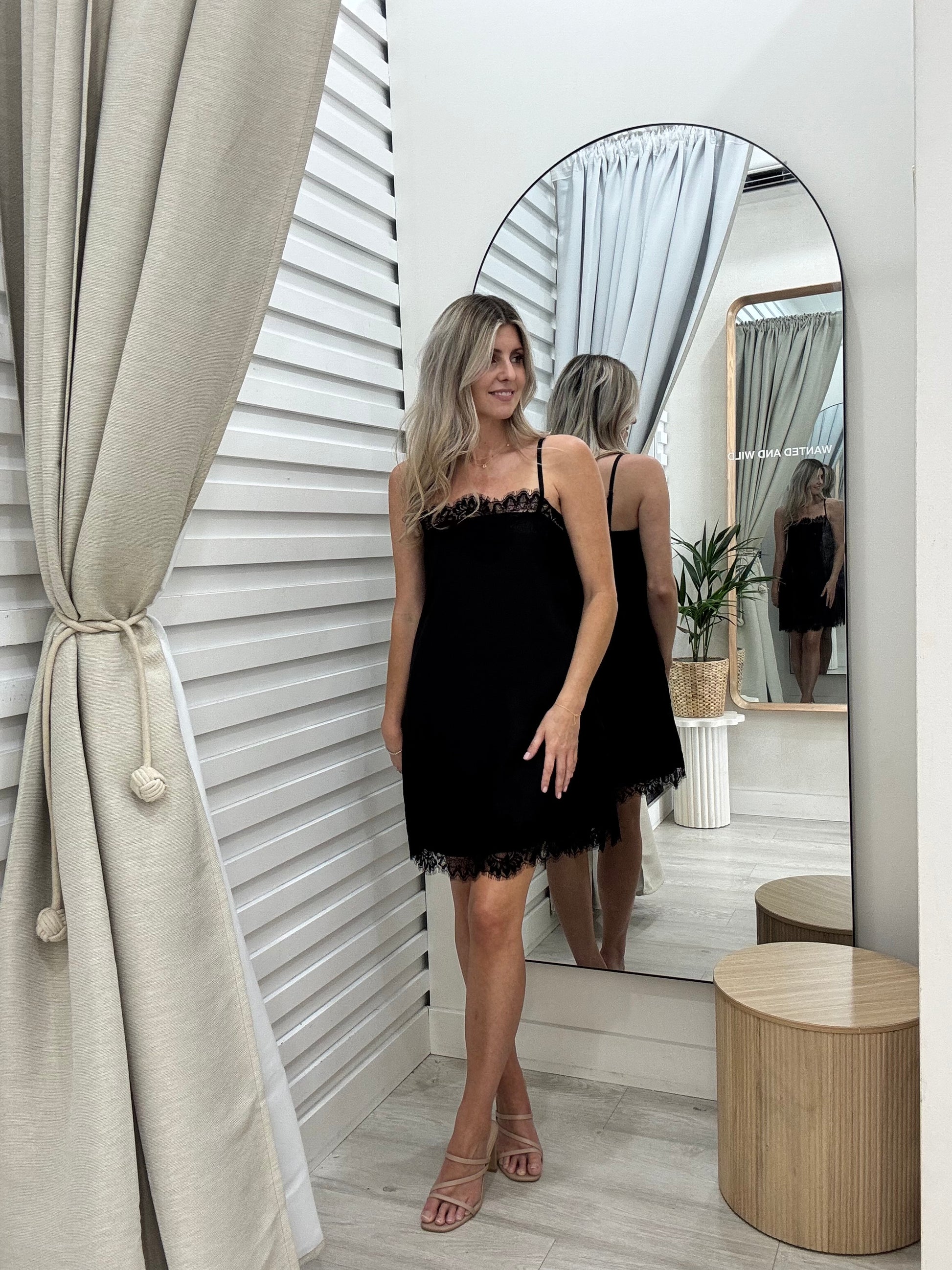 A woman in the Ace dress in black. By Frankie label standing in front of a mirror in the changeroom of Wanted and Wild Gymea.