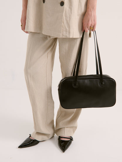 Model holding a black handbag wearing a beige outfit on a white background at Wanted and Wild