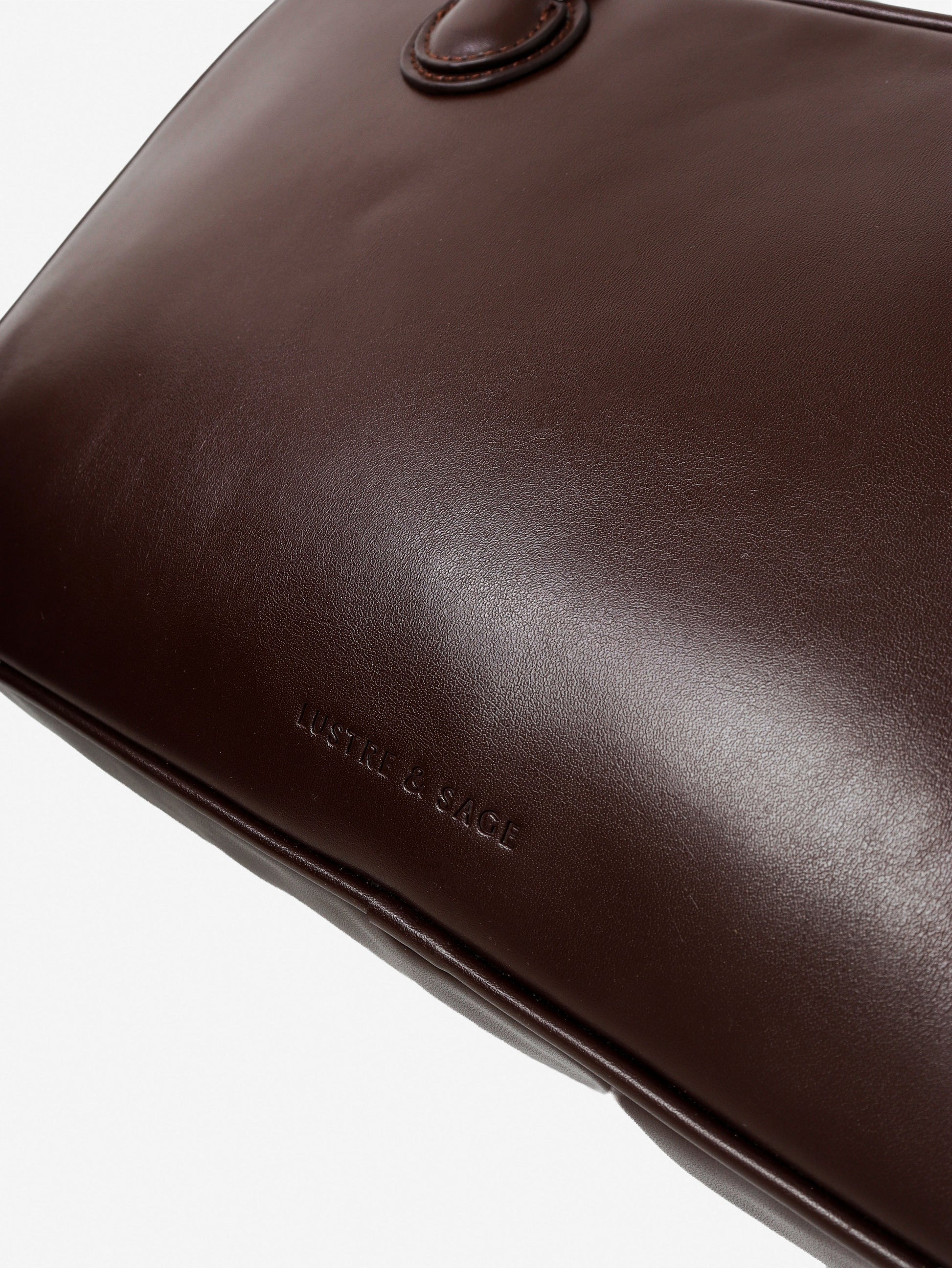 Close-up of a brown leather bag with 'Lustre and Sage' branding on a white background