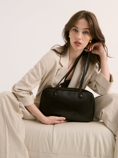 Woman holding a black handbag against a neutral background