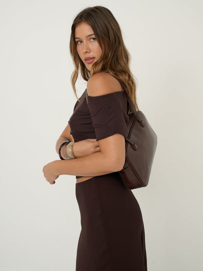 Woman in a brown dress holding a brown handbag against a white background