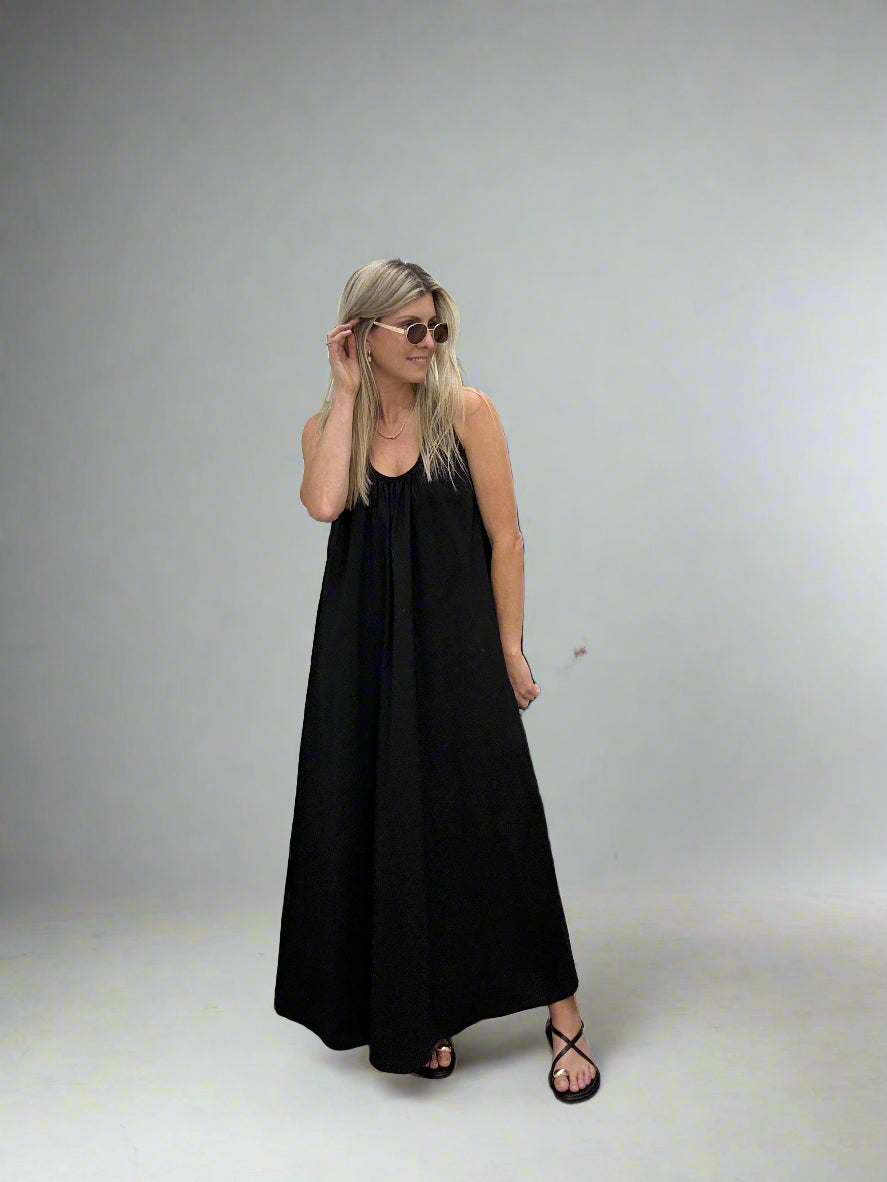 Woman in a black dress standing in front of a mirror in a room with neutral decor.