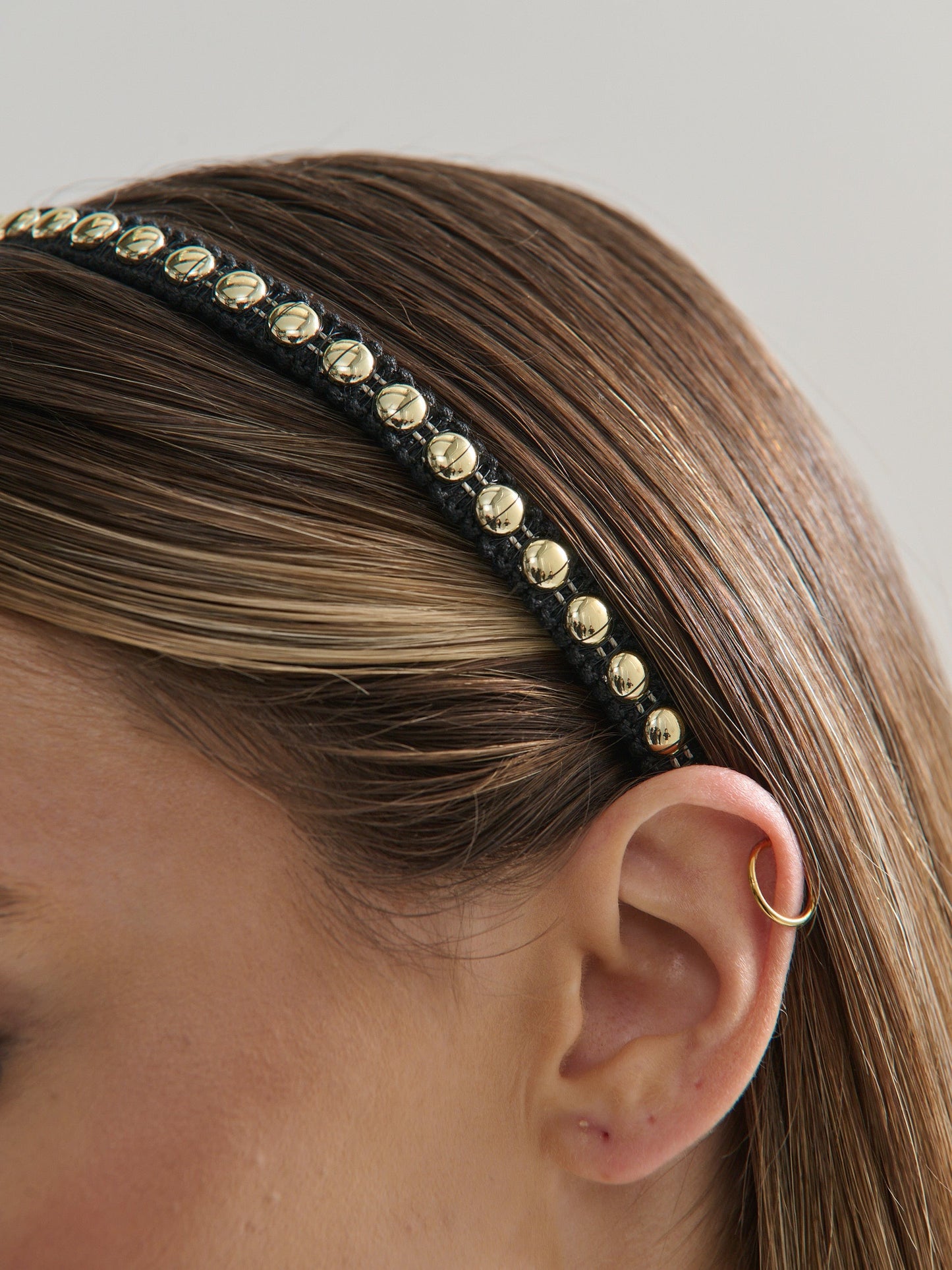 Black headband with gold studs worn by a person, with a neutral background