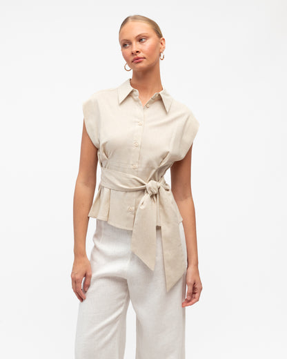 Model wearing a Linen Luxe sleeveless shirt with a tie waist and white pants on a light gray background. White Closet at Wanted and Wild 