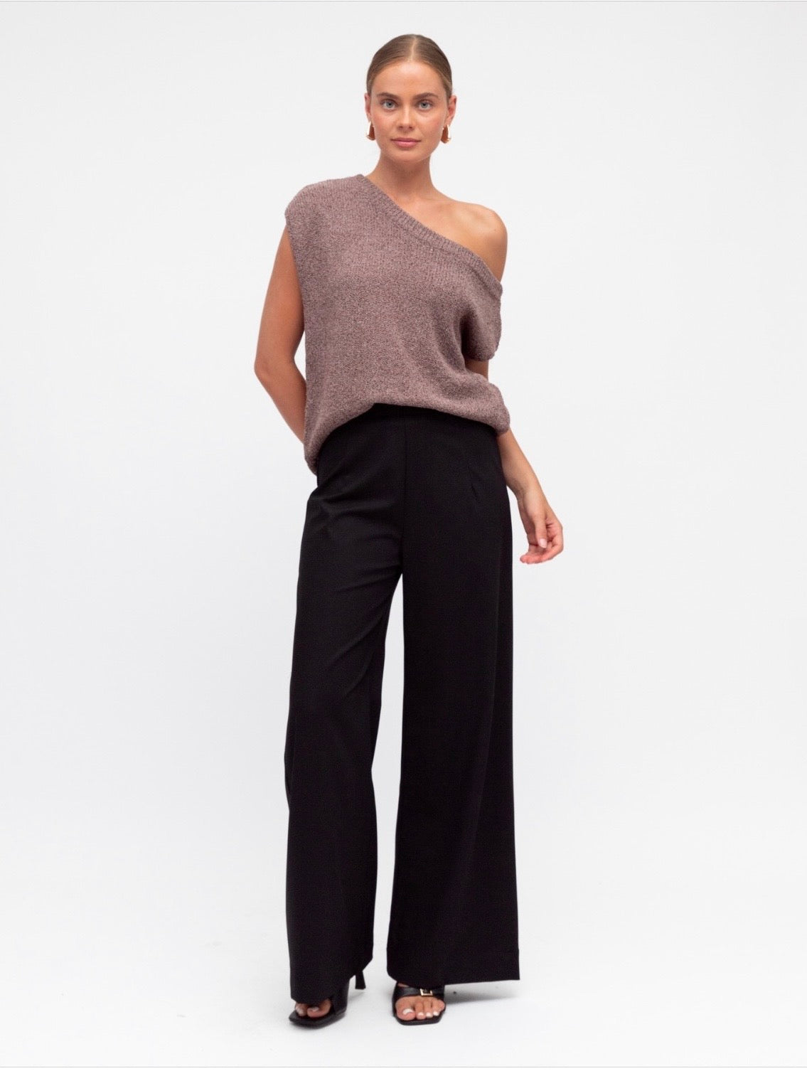 Woman wearing a one-shoulder brown top and black pants on a white background
