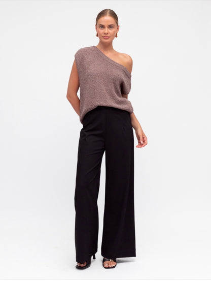Woman wearing a one-shoulder brown top and black pants on a white background