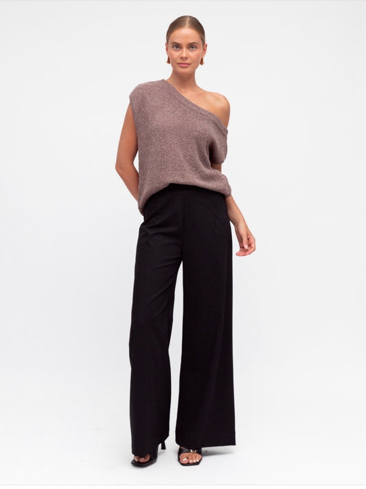 Woman wearing a one-shoulder brown top and black pants on a white background