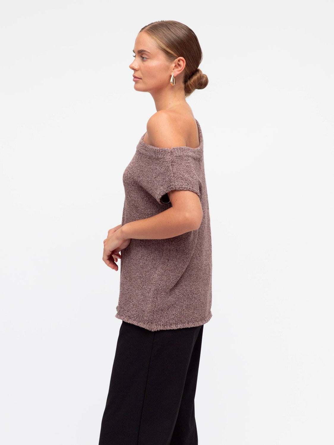 Woman wearing a brown off-shoulder top and black pants on a white background