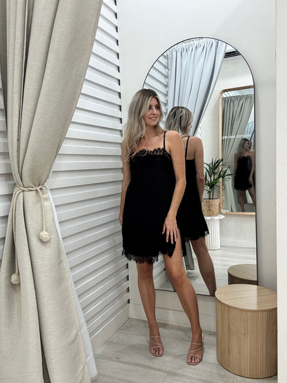 Woman in The Ace dress in black, standing in front of a mirror  at Wanted and Wild. Wearing Brooklyn heels in nude at Wanted and Wild.