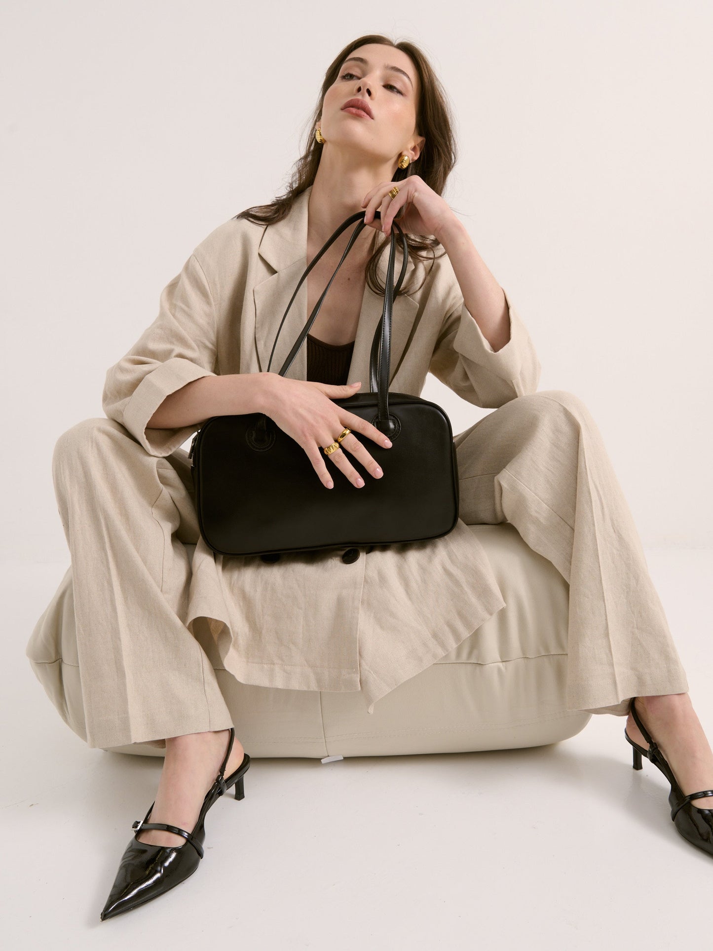 Woman holding a black handbag wearing a beige outfit on a white background